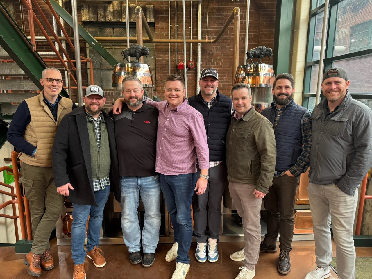 Eight JS Bull Reserve trip attendees together in front of Buffalo Trace barrels on the Weller Full Proof selection trip.