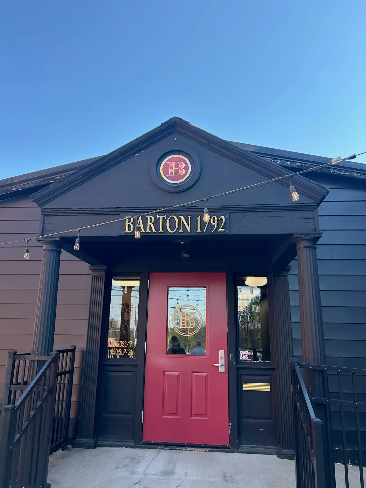 The red door of the Barton 1792 visitor entrance beneath a blue sky.
